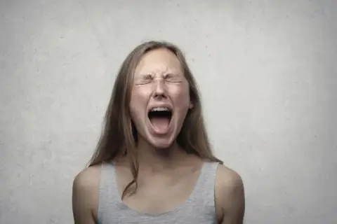 Ragazza con apparecchio dentale urla, occhi chiusi e fronte corrugata, un'espressione di pura paura di perdere il controllo.